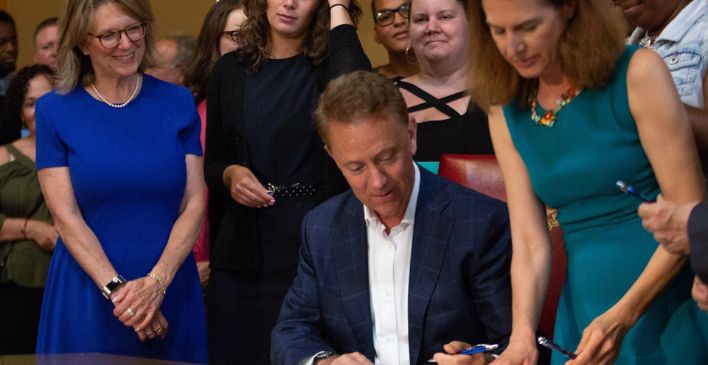 Governor Lamont signing document surrounded by people