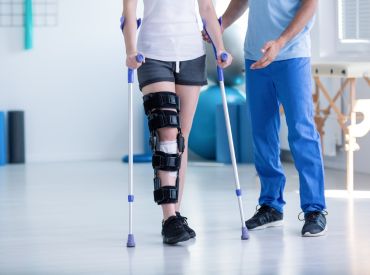 Person with brace on leg walking with crutches 