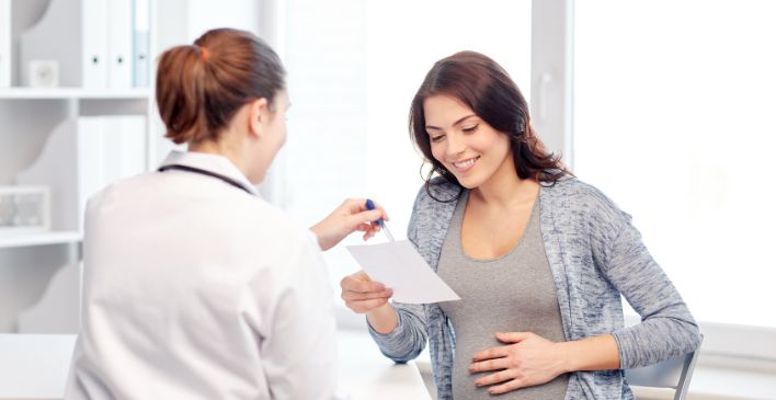 Pregnant woman with hand on stomach talking to doctor