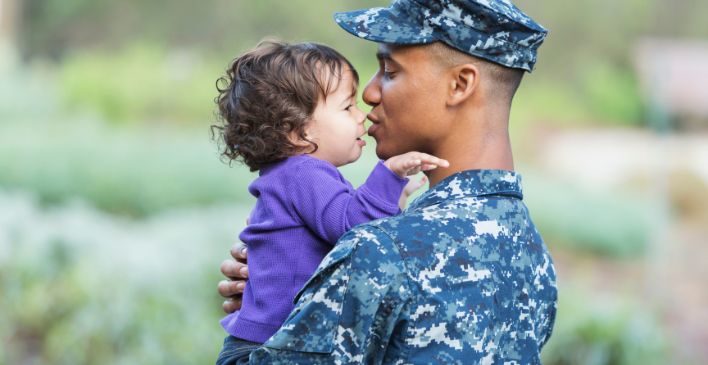 Father in military uniform holding young child