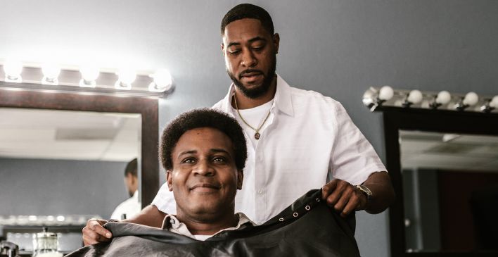 Barber putting gown around a client 